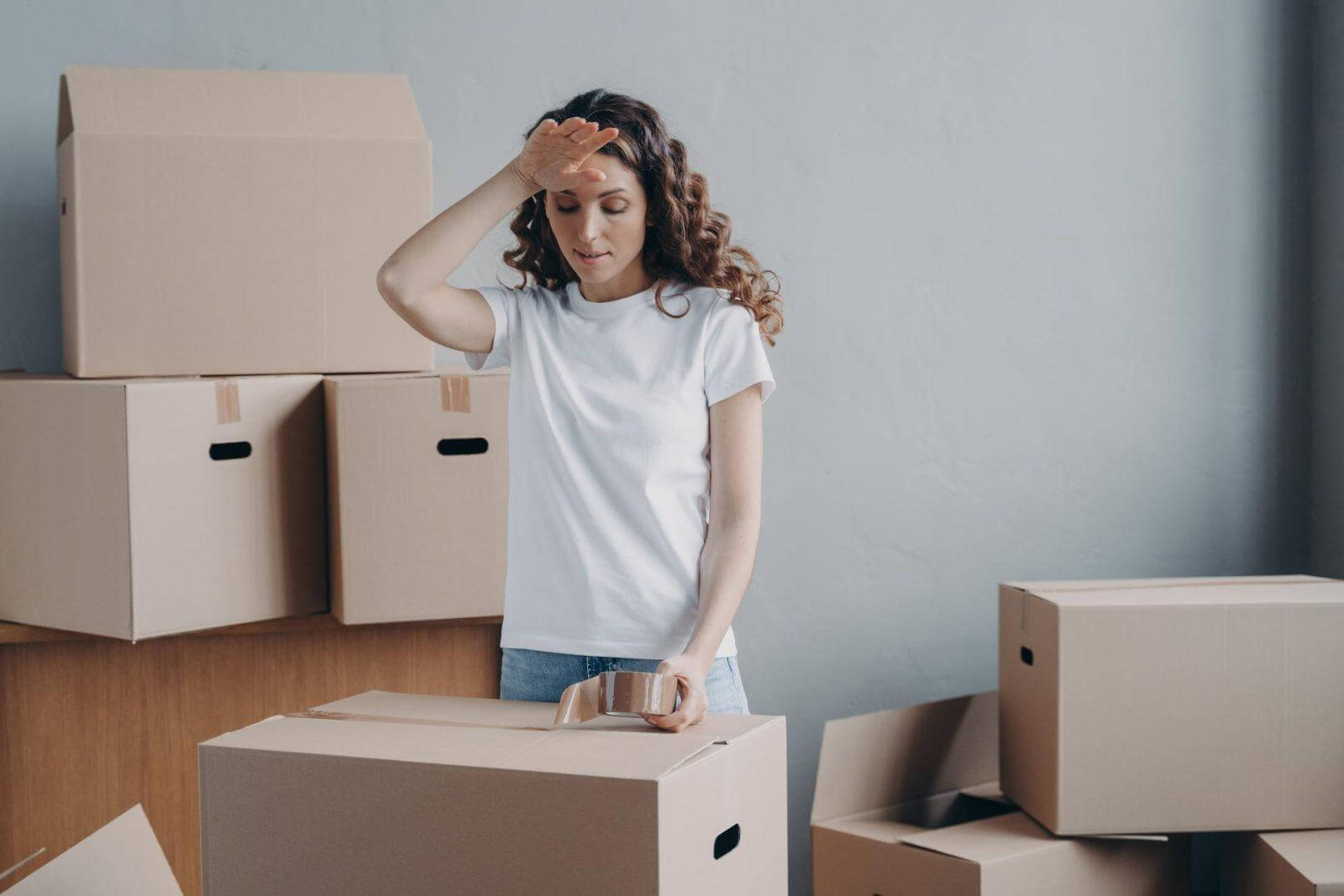 Tired woman packing cardboard box with things, preparing to relocation to new home. Hard moving day.