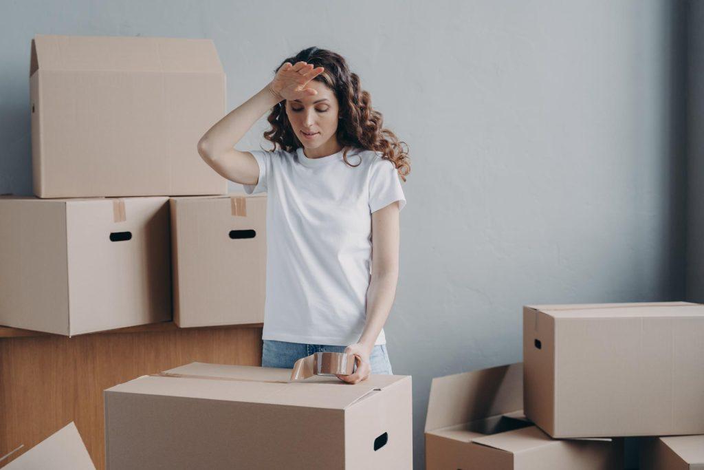 Tired woman packing cardboard box with things, preparing to relocation to new home. Hard moving day