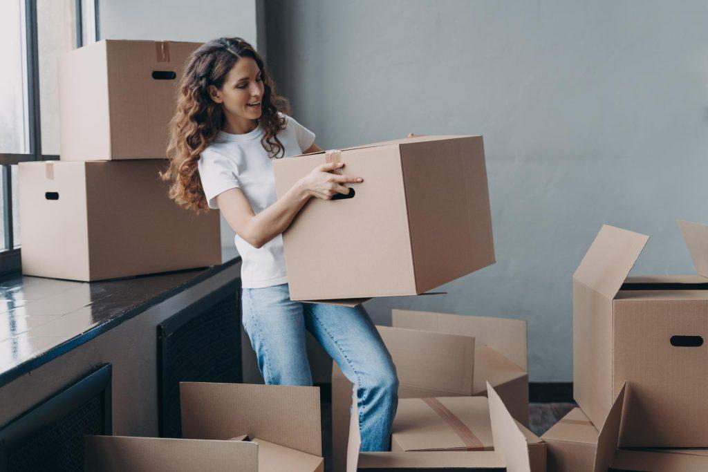 Young lady in white t-shirt is carrying cardboard box. Hispanic woman packing things and leaving.